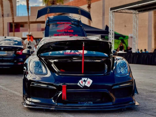 Custom Porsche Cayman with deep lip forged wheels, showcasing a sleek black design and performance modifications at a car event.