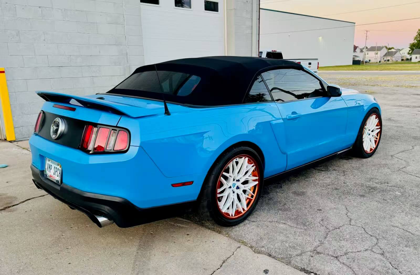 Ford Mustang with custom white and orange wheels, showcasing a vibrant blue exterior and black convertible top.