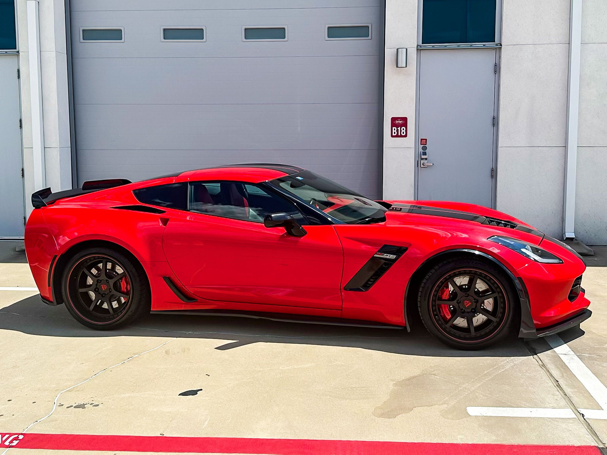 Red Corvette C7 Z06 with custom black and red aftermarket wheels parked outside.