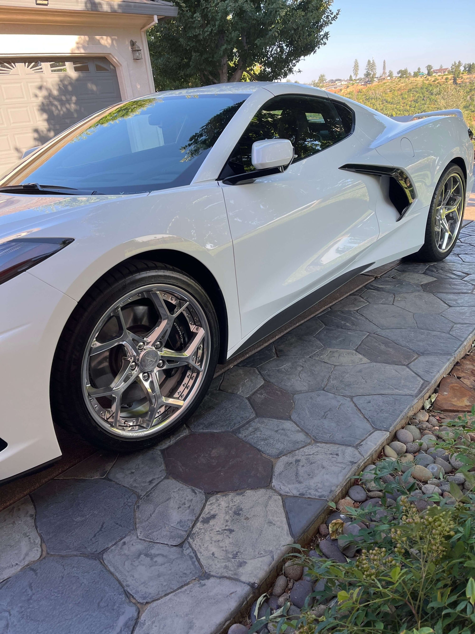 Corvette C8 featuring polished aluminum aftermarket wheels on a sunny driveway.