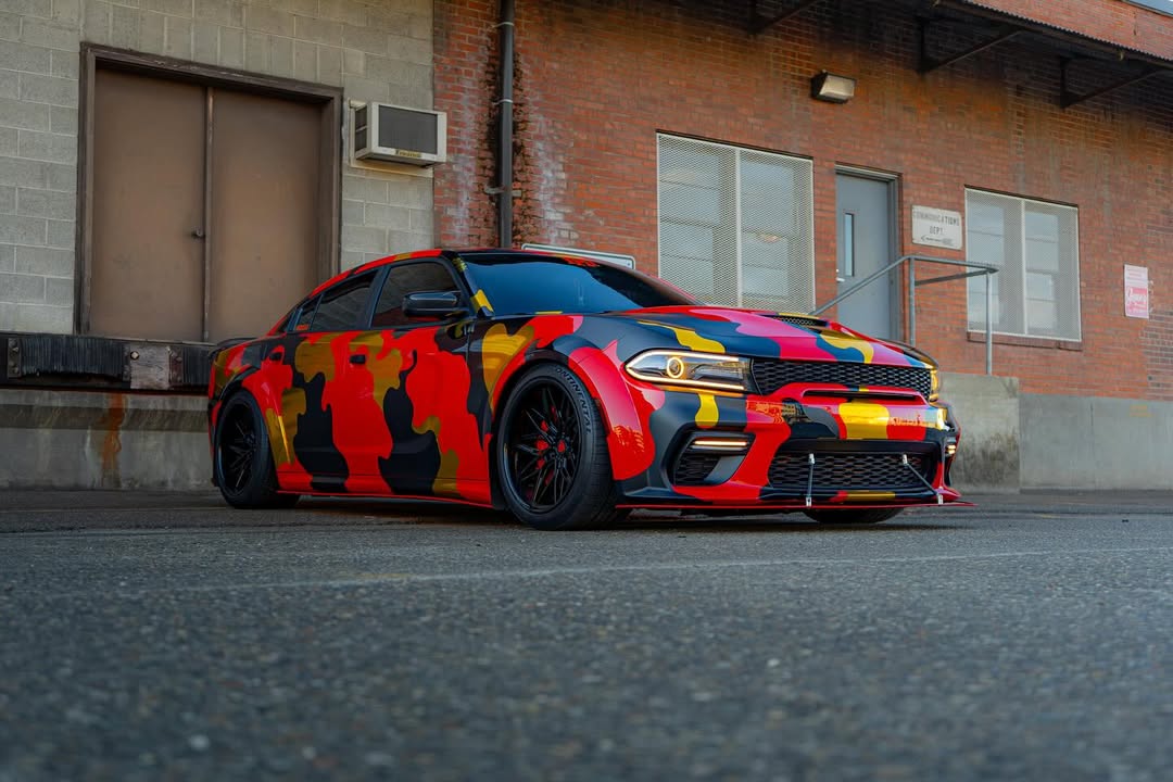 Custom Dodge Charger with 20-inch black deep dish wheels and a vibrant camo wrap parked in an urban setting.