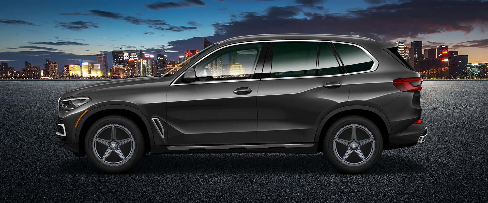 Black BMW X5 SUV parked at night with city skyline in the background, showcasing custom forged wheels.