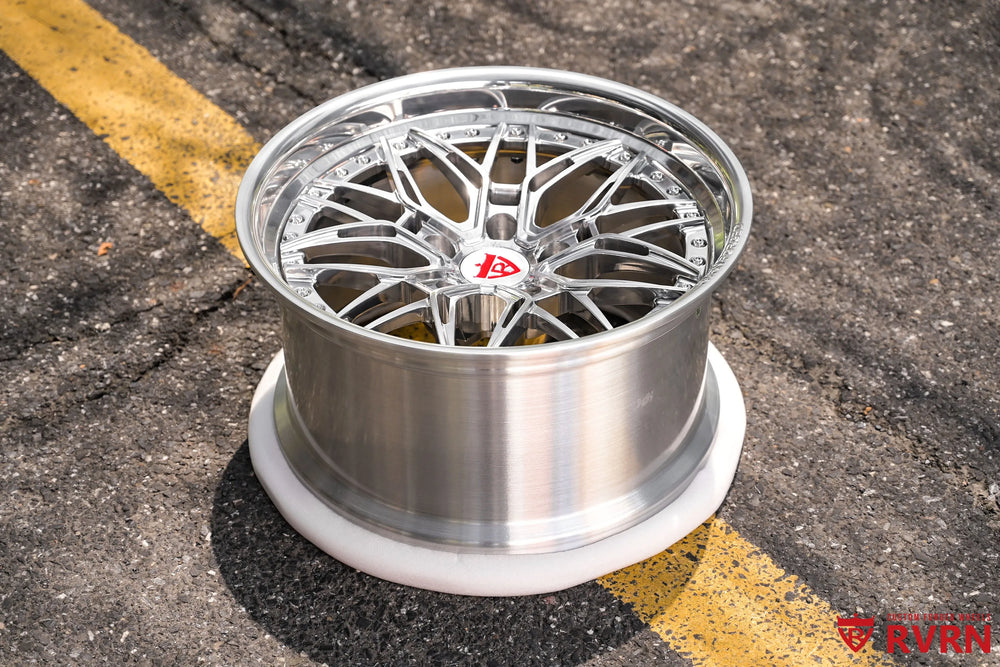 1970 Chevy Nova RV-T081 2-piece forged Y-Spoke Deep Dish wheel with Polished Spoke, Polished Flange, Polished Barrel, and RVRN Red Screws, shown in an elevated outdoor view on asphalt with the polished spoke structure, deep barrel, red center emblem, and contrasting yellow road marking in the background.