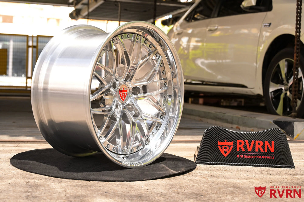 1970 Chevy Nova RV-T081 2-piece forged Y-Spoke Deep Dish wheel with Polished Spoke, Polished Flange, Polished Barrel, and RVRN Red Screws, shown at a three-quarter angle beside a vehicle and RVRN sign with the deep dish depth, polished wheel face, red flange screws, and workshop setting visible.