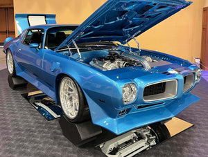 Front three-quarter view of a blue 1973 Pontiac Firebird Trans Am on RVRN RV-DS74 deep dish wheels with the hood open at an indoor show