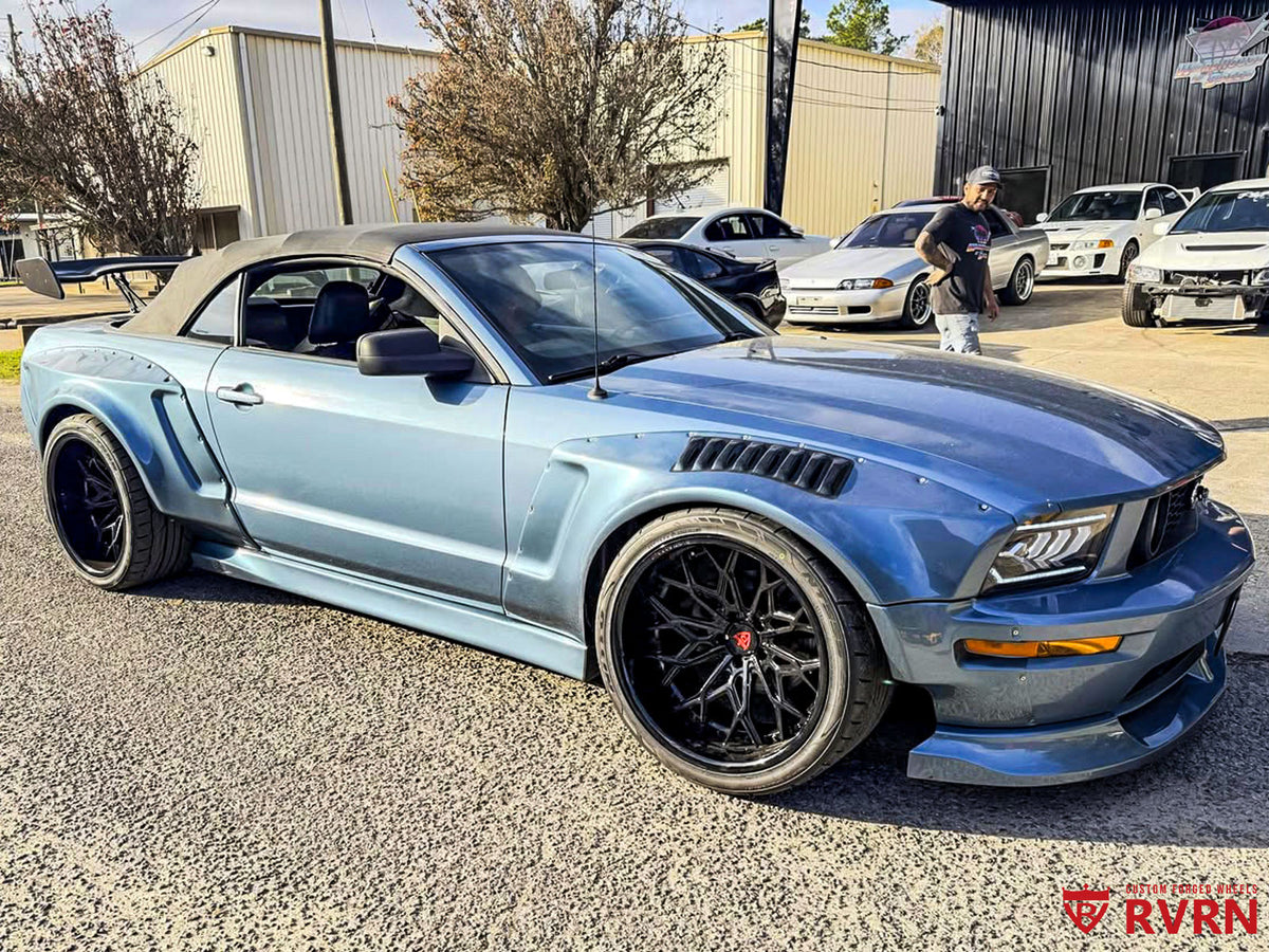 Front three-quarter view of a light blue 2005 Ford Mustang GT convertible on RVRN RV-DN02 deep dish gloss black wheels