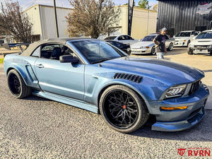 Front three-quarter view of a light blue 2005 Ford Mustang GT convertible on RVRN RV-DN02 deep dish gloss black wheels