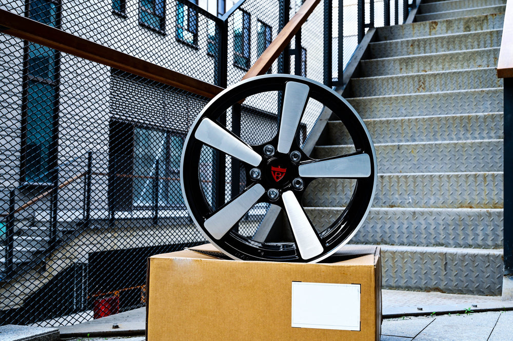 RVRN RV-MP223 5 spoke forged wheel for a 2011 Chevy Camaro LT displayed on a box near a metal staircase, showing the brushed spoke finish against gloss black.