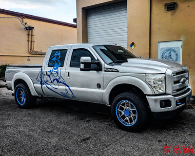 2012 Ford F250 Super Duty on RVRN RV-DR08D custom forged wheels, side profile in front of the Metal Productions building showing the blue chrome wheels and pin-up graphics.