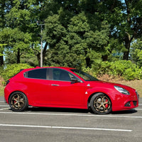 Red Alfa Romeo with bronze custom forged wheels parked under trees, showcasing custom wheels and stylish design.