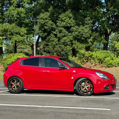 Red Alfa Romeo with bronze custom forged wheels parked under trees, showcasing custom wheels and stylish design.