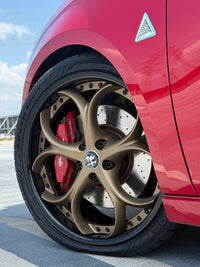 Close-up of an Alfa Romeo with bronze custom forged wheels and sleek red paint, showcasing unique custom rims.