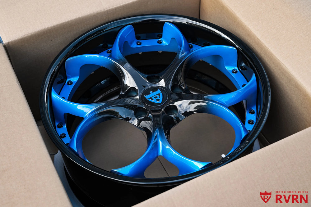 2015 Corvette C7 Z51 RV-DS016 custom forged 2-piece wheel resting inside a cardboard box, viewed from above to show the blue and black two-tone spokes, center cap, deep barrel, and assembly hardware