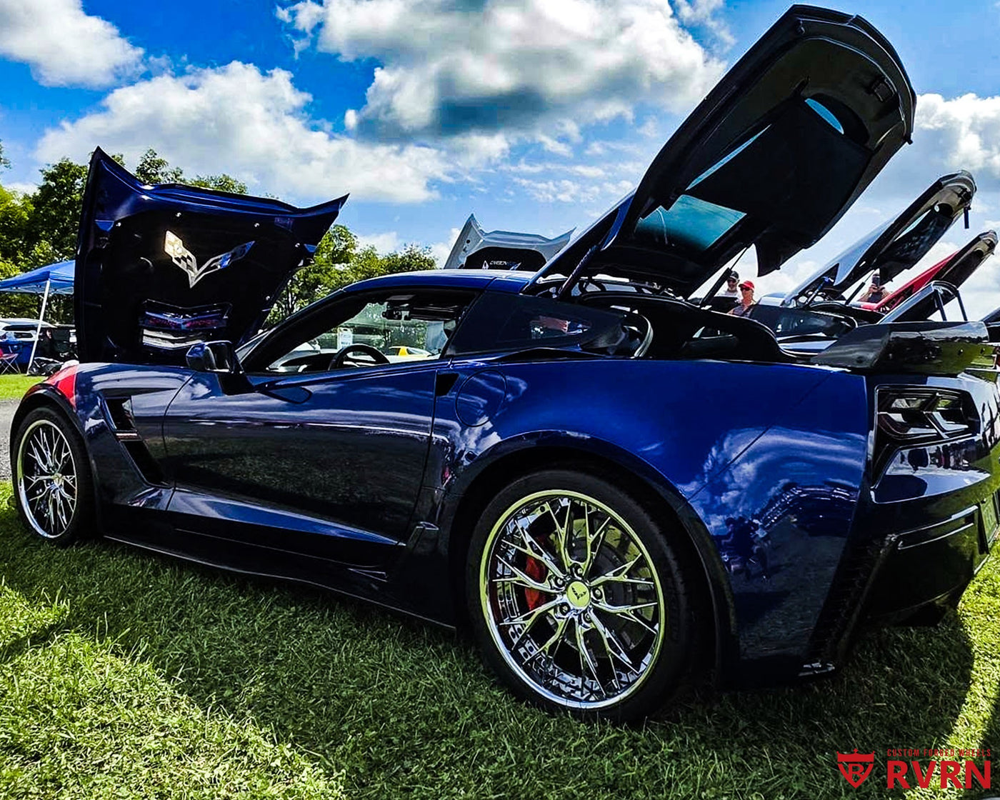 Metallic blue 2017 Corvette C7 Grand Sport on RVRN RV-DC04 chrome custom forged wheels with dark blue screws, displayed at a Corvette car show with hood and hatch open.