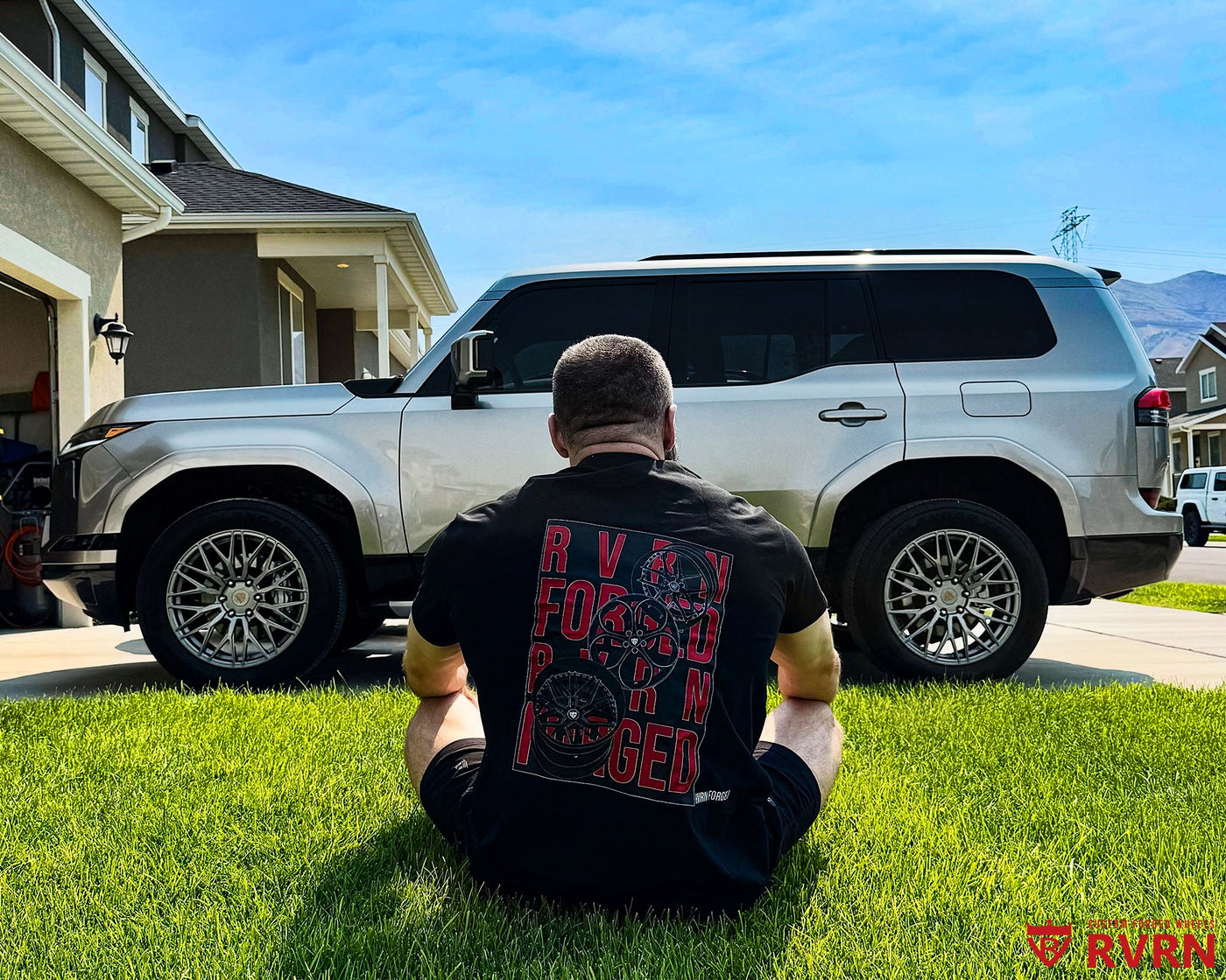 2026 Lexus GX 550 on RVRN RV-MG122 custom forged wheels in Gloss Gunmetal, owner in RVRN FORGED shirt sitting on the lawn beside the SUV.