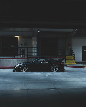 Side profile of a 2014 Porsche Cayman widebody on RVRN RV-DP02 5 spoke polished aluminum forged wheels in a parking garage.