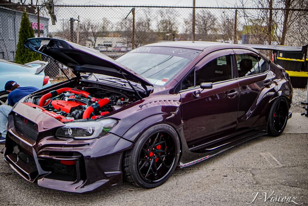 Modified Subaru WRX with custom black deep dish wheels and red engine details, showcasing unique wheel designs.