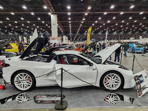 White Corvette C8 showcasing custom aftermarket wheels and rims at a car show, featuring eye-catching design and detailing.