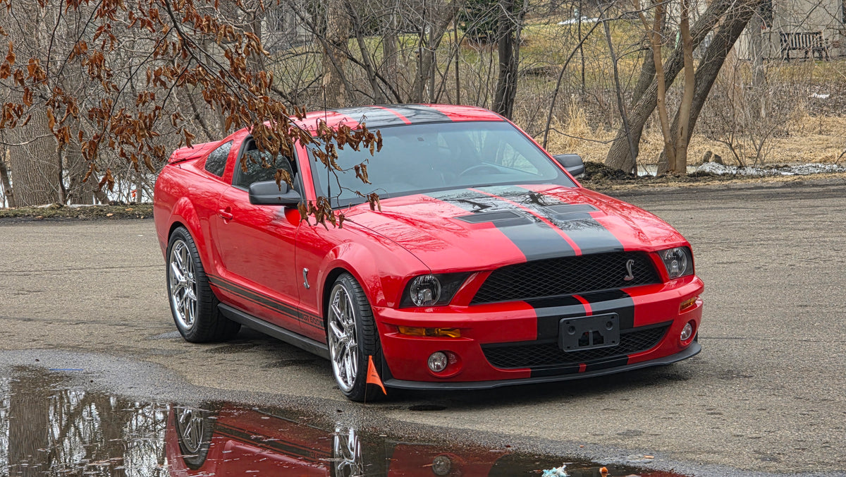 Red 2008 Ford Mustang GT500 with black stripes parked on a street