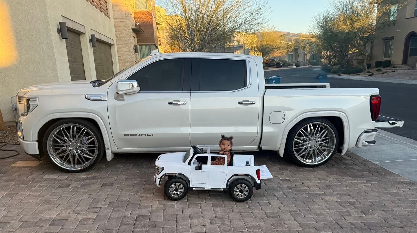 Large white GMC series 1500 pickup truck with a smaller toy truck on a brick driveway.
