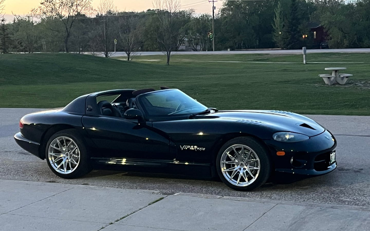 Black viper sports car parked on a paved surface with grass and trees in the background