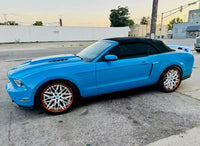 Ford Mustang with custom white and orange rims parked on the street, showcasing vibrant blue exterior and convertible design.