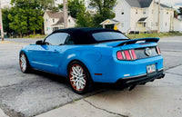 Ford Mustang with custom white and orange rims parked on a street, showcasing its stylish design and vibrant color.