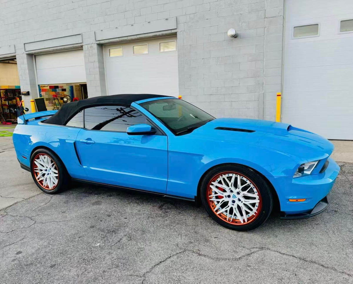 Ford Mustang with custom white and orange rims, showcasing a vibrant blue exterior and convertible top.
