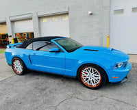 Ford Mustang with custom white and orange rims, showcasing a vibrant blue exterior and convertible top.