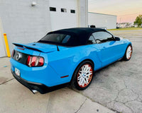 Stylish blue Ford Mustang convertible featuring custom white and orange rims, showcased in a parking lot.