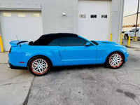Ford Mustang with custom white and orange rims parked in front of a garage.