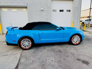 Ford Mustang with custom white and orange rims parked in front of a garage.