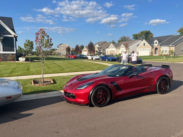 Red sports car parked on a residential street with houses and trees in the background.