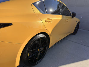 Rear three-quarter view of a yellow 2025 Lexus IS500 on RVRN RV-DC24 gloss black concave wheels with yellow screws, driveway setting