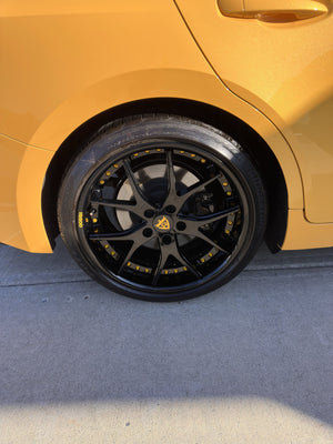 Front wheel close-up of a 2025 Lexus IS500 on RVRN RV-DC24 gloss black forged wheels with yellow screws and IS500 tire lettering