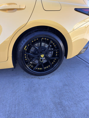 Overhead close-up of the rear RVRN RV-DC24 gloss black wheel with yellow screws on a yellow 2025 Lexus IS500 in a garage