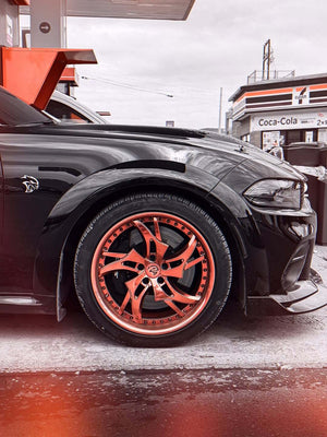 Close-up of the rose gold RVRN RV-DC39 deep dish wheel and Hellcat badge on a black 2023 Dodge Charger Widebody at a gas station