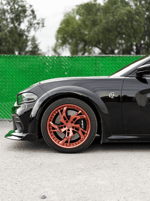Close-up of the rose gold RVRN RV-DC39 deep dish wheel on a black 2023 Dodge Charger Widebody, green fence background