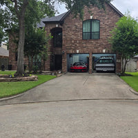 Modern brick house with a Corvette C8 and a truck in the driveway under a clear sky.