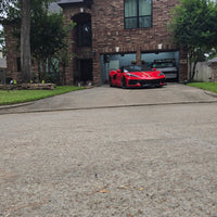 Red Corvette C8 with custom RVRN forged matte bronze wheels parked in driveway of a brick house.