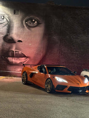 Front three-quarter view of an orange 2024 Corvette C8 Stingray on RVRN RV-DR08 deep dish gold chrome wheels, night mural backdrop