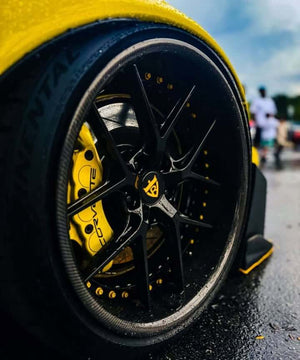 Close-up of the RVRN RV-DR08D gloss black forged wheel with carbon fiber lip and yellow Corvette brake caliper, rain droplets