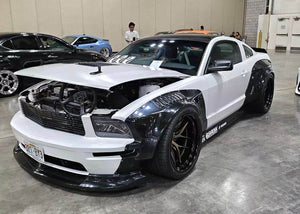Front three-quarter view of a white 2007 Ford Mustang Widebody with gloss bronze RVRN RV-DR08D wheels at an indoor car show