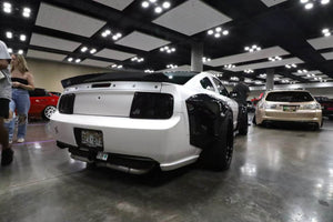 Rear three-quarter view of a white 2007 Ford Mustang Widebody on RVRN RV-DR08D deep dish bronze wheels inside a convention hall