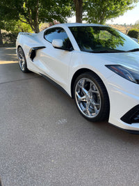 Close-up of a white Corvette C8 showcasing polished aluminum aftermarket wheels on a driveway.