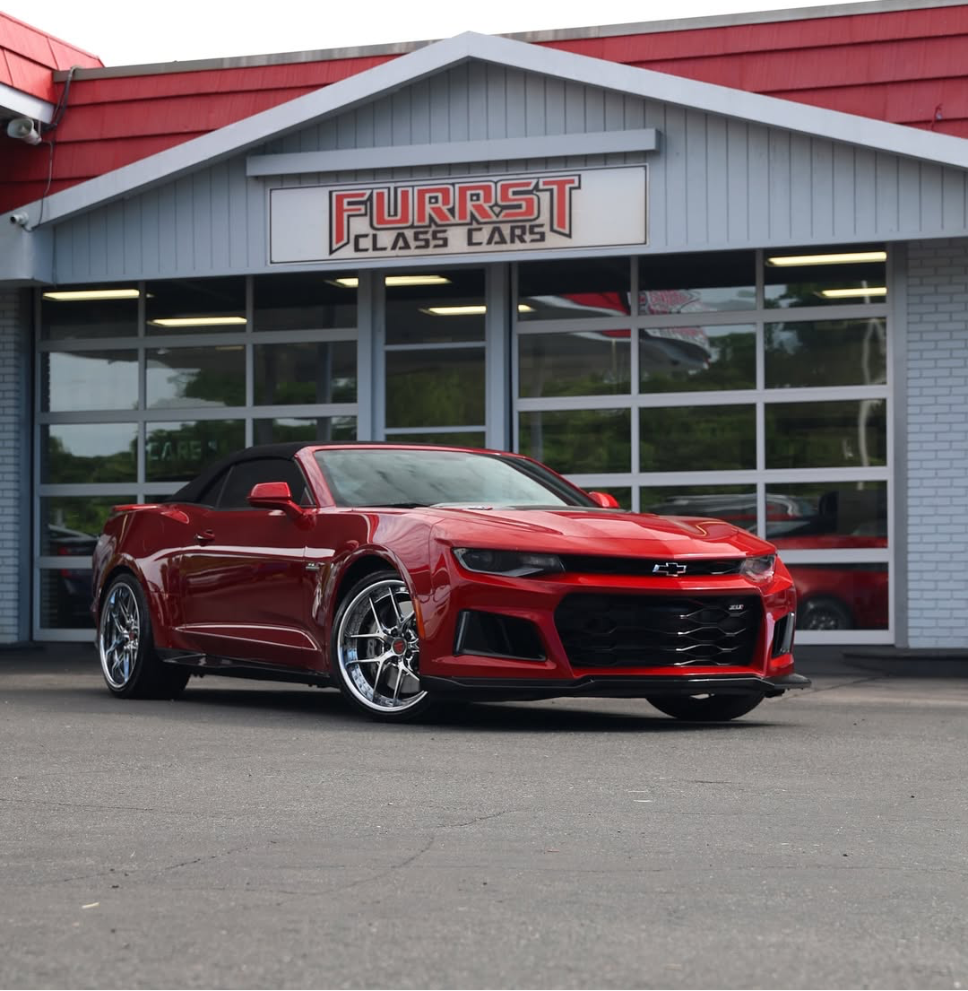 A red Chevrolet Camaro convertible with chrome rv-dr08 forged wheels is parked in front of a dealership building with a large sign reading 'FURRIST CLASS CARS'.