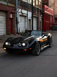 1973 C3 Corvette convertible with custom chrome and red aluminum wheels parked on urban street.
