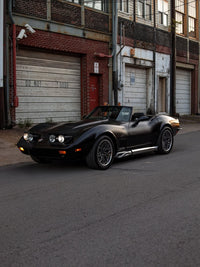 1973 C3 Corvette with custom 18 inch chrome and red rims parked on a street in front of a warehouse.