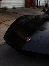 Close-up of a 1973 C3 Corvette with custom chrome and red rims, showcasing its sleek design and distinctive emblem.