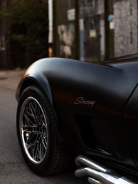 Close-up of a 1973 Corvette Stingray featuring sleek chrome wheels and a stylish matte black finish.